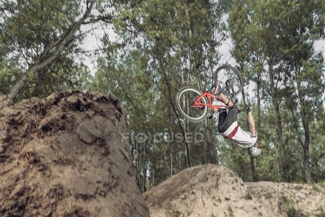 Piloto realizando flip over com bicicleta na floresta — Fotografia de Stock